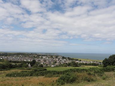 A coastal town with houses fields and the sea under a partly cloudy sky at Glan Awel in Nefyn
