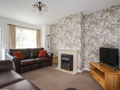 A living room with dark brown leather sofas a fireplace a wooden TV stand with a TV and floral wallpaper at Glan Awel in Nefyn