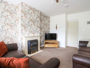 A living room with a fireplace floral wallpaper two brown sofas and a television on a wooden stand at Glan Awel in Nefyn