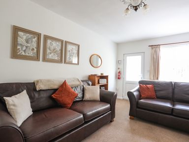 A living room with two leather sofas cushions framed botanical prints a small wooden shelf a round mirror and a door with a window at Glan Awel in Nefyn