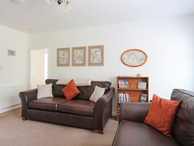 A living room with brown leather sofas and cushions a small bookshelf and framed pictures on the wall at Glan Awel in Nefyn