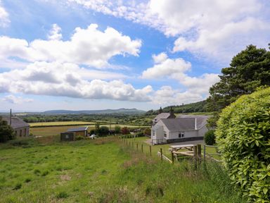 A rural landscape with a white house a fenced grassy yard and rolling hills in the background at Glan Awel in Nefyn