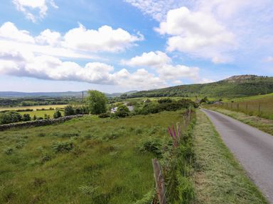 A rural road with grass and fences on both sides and hills in the background at Glan Awel in Nefyn