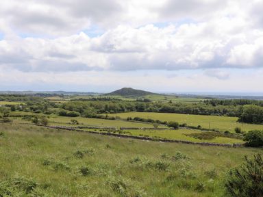 A green rural landscape with fields trees and stone walls under a cloudy sky at Glan Awel in Nefyn