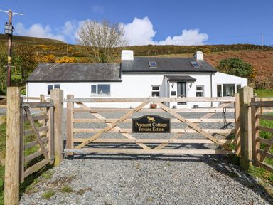 A wooden gate with a sign reading Pennant Cottage Private Estate and a white cottage behind it at Pennant Cottage in Llithfaen