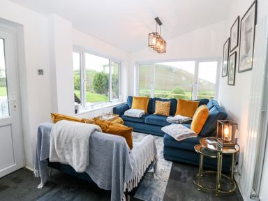 A sitting room with blue sofas orange cushions and blankets with a side table and lamp at Pennant Cottage in Llithfaen