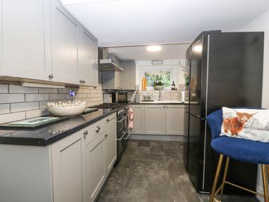 A kitchen with grey cabinets black appliances and a blue chair with a cushion at Pennant Cottage in Llithfaen
