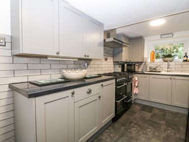 A kitchen with grey cabinets black countertop and a black stove at Pennant Cottage in Llithfaen