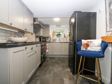 A kitchen with grey cabinets black refrigerator blue bar stool with animal pillow at Pennant Cottage in Llithfaen