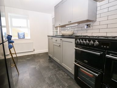 A kitchen with grey cabinets black oven blue high stools and a window at Pennant Cottage in Llithfaen