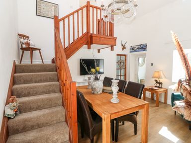 A dining area with a wooden table and black chairs next to a carpeted staircase and wooden railing at Pennant Cottage in Llithfaen