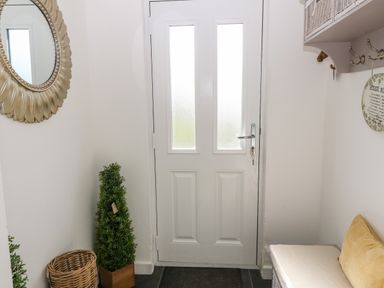 An entryway with a white door a round mirror a basket a small plant and a bench with a cushion at Pennant Cottage Llithfaen