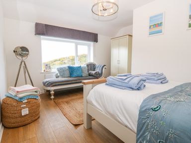 A bedroom with a bed folded towels a striped chaise lounge a wardrobe and a tripod lamp at Pennant Cottage in Llithfaen