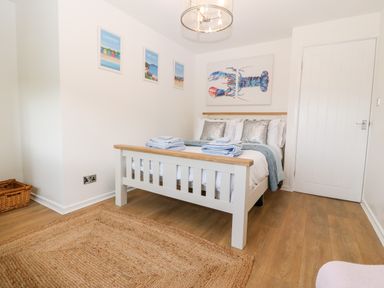 A bedroom with a white bed and folded towels on a wooden floor at Pennant Cottage in Llithfaen