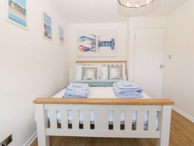 A bedroom with a white wooden double bed with folded towels on it and a lobster painting on the wall at Pennant Cottage in Llithfaen