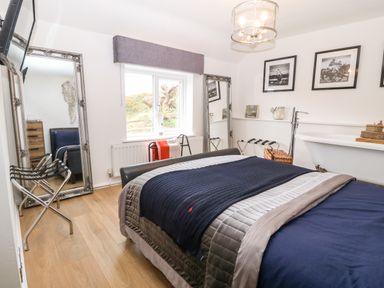 A bedroom with a bed a freestanding bathtub two full length mirrors and framed pictures on the wall at Pennant Cottage in Llithfaen