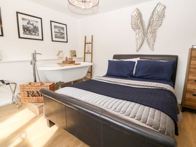 A bedroom with a black leather bed blue bedding a white freestanding bathtub wooden ladder and basket at Pennant Cottage in Llithfaen