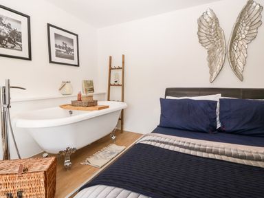 A bedroom with a bed with dark blue bedding and a white freestanding bathtub with claw feet at Pennant Cottage in Llithfaen