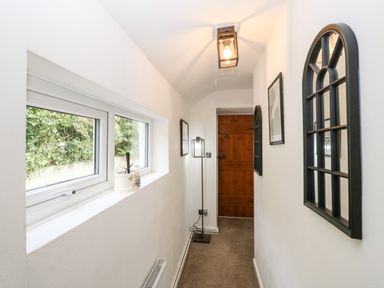A narrow hallway with a wooden door at the end a window on the left and decorative black framed mirrors on the right wall at Pennant Cottage in Llithfaen