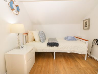 A bedroom with a single bed a bedside table with a lamp and hardwood floor at Pennant Cottage in Llithfaen