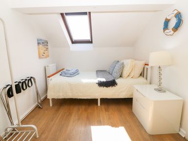 A bedroom with a single bed a bedside table with a lamp and a wall window at Pennant Cottage in Llithfaen