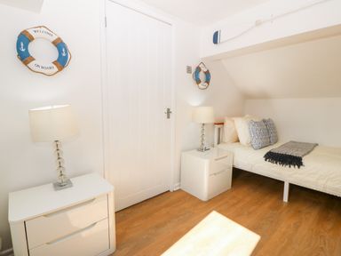 A bedroom with a single bed pillows and throw blankets two bedside tables with lamps and life preserver wall decor at Pennant Cottage in Llithfaen