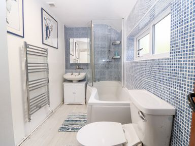 A bathroom with a bathtub shower combination sink toilet towel rack and two framed pictures at Pennant Cottage in Llithfaen