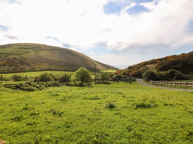 A grassy field with hills in the background and a gravel path with fences at Pennant Cottage in Llithfaen