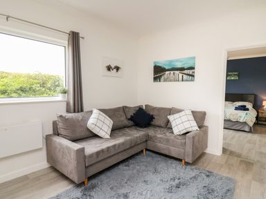 A living room with a grey sectional sofa and two paintings on the wall at Ty Cariad in Llangynin near St Clears