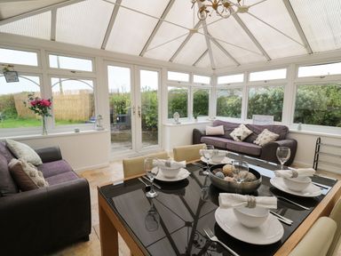 A conservatory with a glass roof two sofas and a dining table set for four at Ty Cariad in Llangynin near St Clears