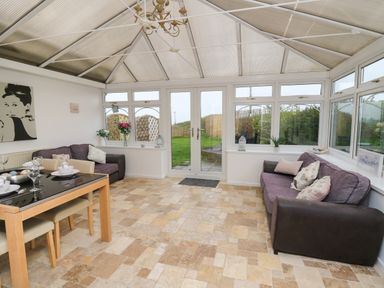 A conservatory with two sofas a dining table set and glass doors leading to a garden at Ty Cariad in Llangynin near St Clears