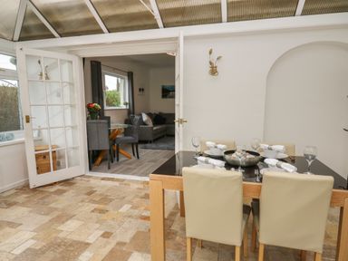A dining area with a glass table set for four and a living room visible through open glass doors at Ty Cariad in Llangynin near St Clears