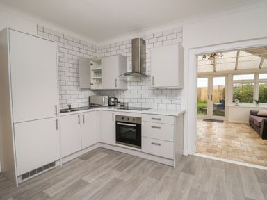 A kitchen with white cabinets a stainless steel oven and hood and a doorway to a sunroom at Ty Cariad in Llangynin near St Clears