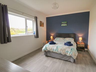 A bedroom with a double bed bedside tables lamps and a window with curtains at Ty Cariad in Llangynin near St Clears