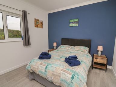 A bedroom with a double bed blue and beige bedding two bedside tables each with a lamp and a window with gray curtains at Ty Cariad in Llangynin near St Clears