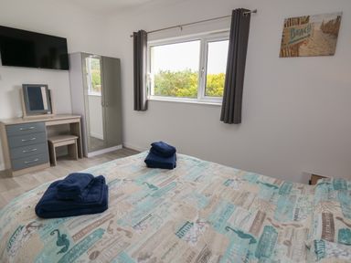 A bedroom with a bed with folded towels a wardrobe a dressing table and a window with curtains at Ty Cariad in Llangynin near St Clears