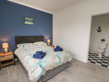 A bedroom with a bed and bedside tables and an open door showing a toilet at Ty Cariad in Llangynin near St Clears
