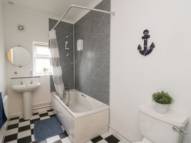 A bathroom with a bathtub shower combination a sink a toilet and a wall decoration at Ty Cariad in Llangynin near St Clears