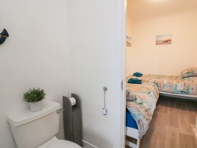 A bathroom with a toilet and a plant on the cistern next to a bedroom with two single beds with patterned bedding at Ty Cariad in Llangynin near St Clears