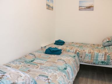 A bedroom with two single beds with patterned bedding and folded towels on each bed at Ty Cariad in Llangynin near St Clears
