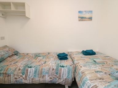 A bedroom with two beds side by side with printed bed covers and folded teal towels on them at Ty Cariad in Llangynin near St Clears
