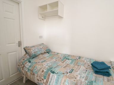 A small bedroom with a single bed covered with printed bedding and folded towels on top at Ty Cariad in Llangynin near St Clears