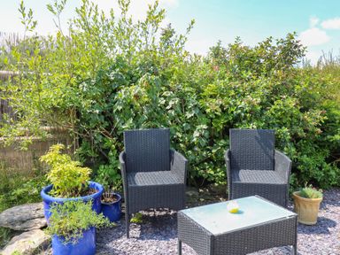 An outdoor seating area with two black wicker chairs and a wicker table with a glass top surrounded by potted plants at Ty Cariad in Llangynin near St Clears