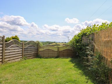 A garden with grass surrounded by wooden fences and vegetation at Ty Cariad in Llangynin near St Clears