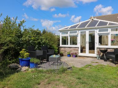 An outdoor patio with black chairs a table potted plants and a barbecue near a conservatory at Ty Cariad in Llangynin near St Clears