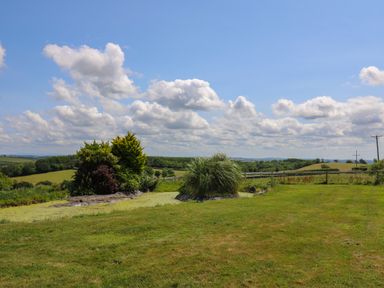 A grassy garden with shrubs and rolling hills in the background at Ty Cariad in Llangynin near St Clears