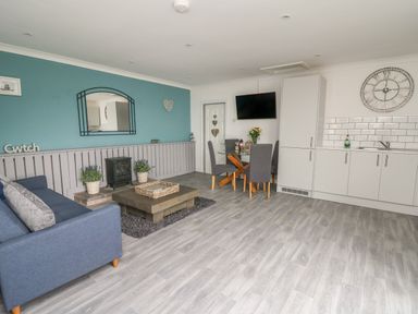 A room with a blue sofa and coffee table blue wall with a mirror dining table with chairs and kitchenette with white cabinets at Ty Cwtch in Llangynin near St Clears