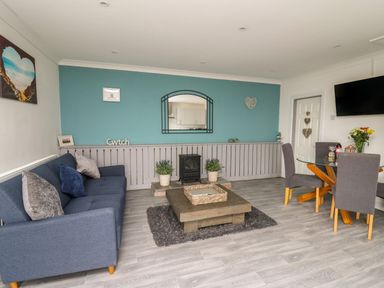 A living room with a blue sofa a wooden coffee table and a dining area with a glass table and gray chairs at Ty Cwtch in Llangynin near St Clears