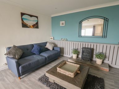 A living room with a blue sofa cushions a wooden coffee table a decorative fireplace and a mirror at Ty Cwtch Llangynin near St Clears
