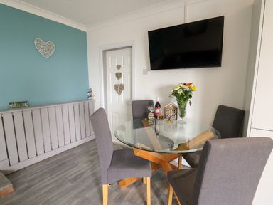A dining area with a glass table and four chairs a wall-mounted tv and a blue and white wall with heart decorations at Ty Cwtch in Llangynin near St Clears